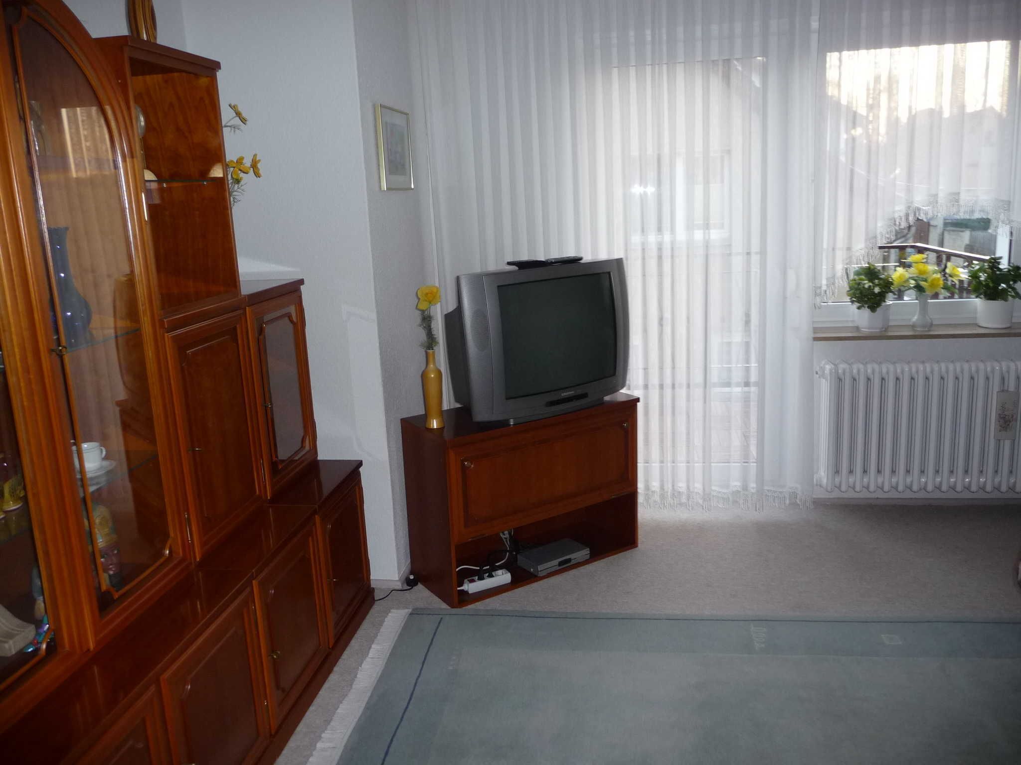 A living room with a wooden cabinet, a television on a stand, a radiator, and a window with curtains.