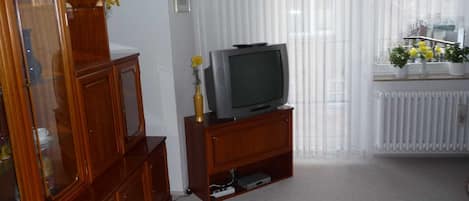 A living room with a wooden cabinet, a television on a stand, a radiator, and a window with curtains.