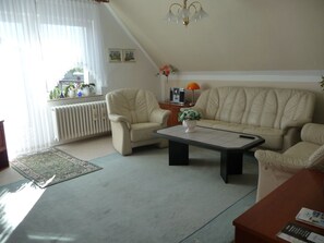 A living room with a sofa, armchair, coffee table, and a radiator. - Apartment OG - Apartment / DZ Blesse Allstedt (Allstedt)