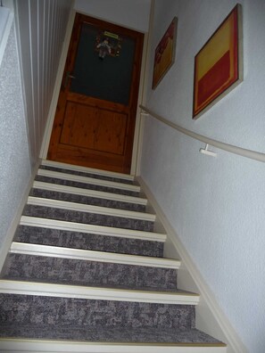 Eine Treppe mit Teppichstufen, eine Holztür und zwei gerahmte Bilder an der Wand.