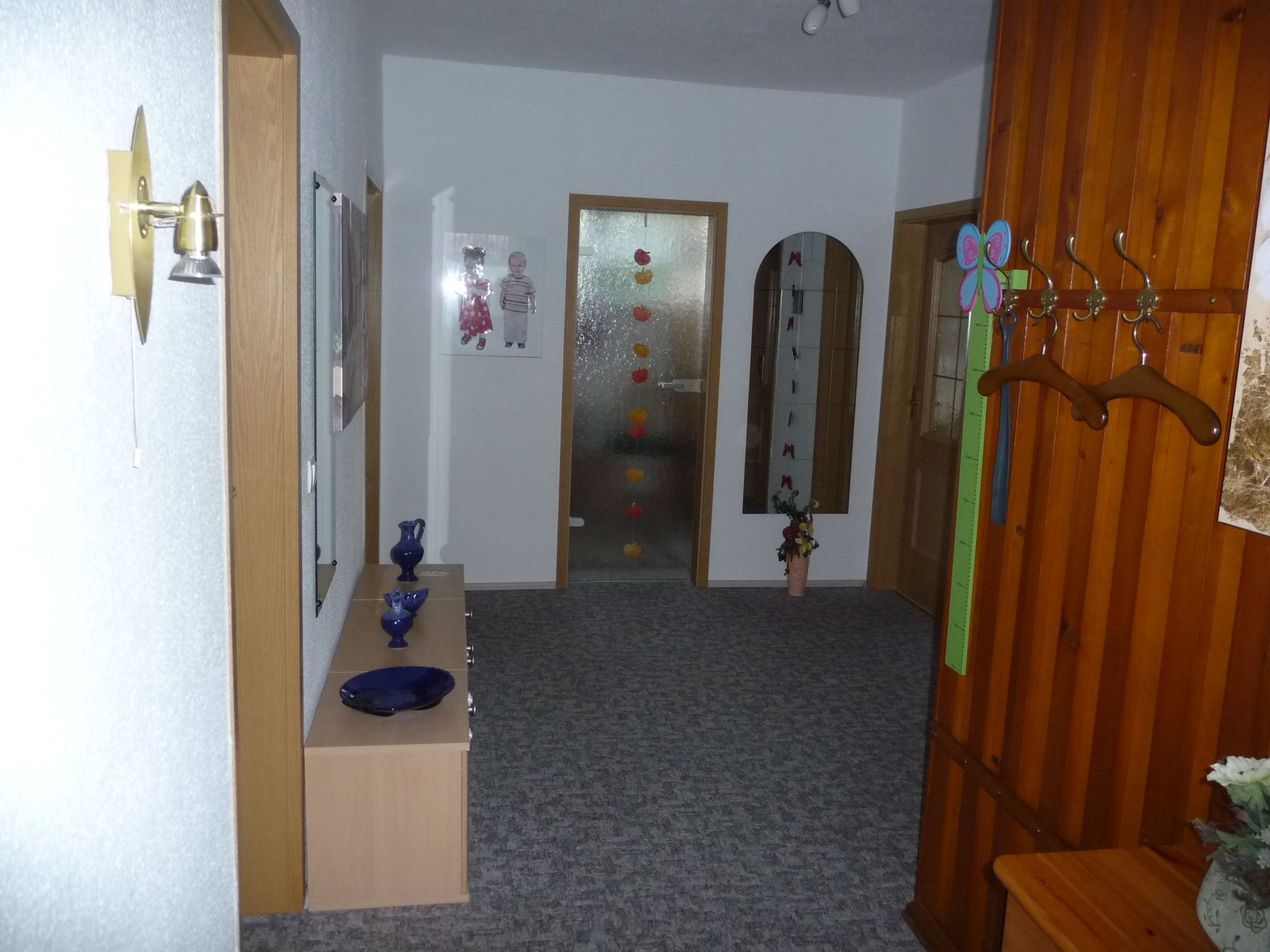 Un pasillo con puerta de madera, espejo, florero y perchero.