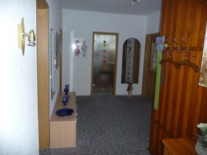 A hallway with a wooden door, a mirror, a vase, and a coat rack. - Apartment OG - Apartment / DZ Blesse Allstedt (Allstedt)