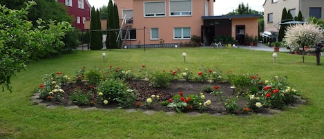 A residential area with a well-maintained garden, solar panels on a house, and a variety of flowering plants.