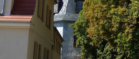A narrow street with a church tower, a parked car, and a tree.