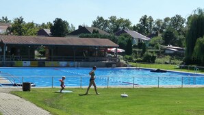 A swimming pool with a grassy area in front, a paved walkway, and houses in the background. - Apartment OG - Apartment / DZ Blesse Allstedt (Allstedt)