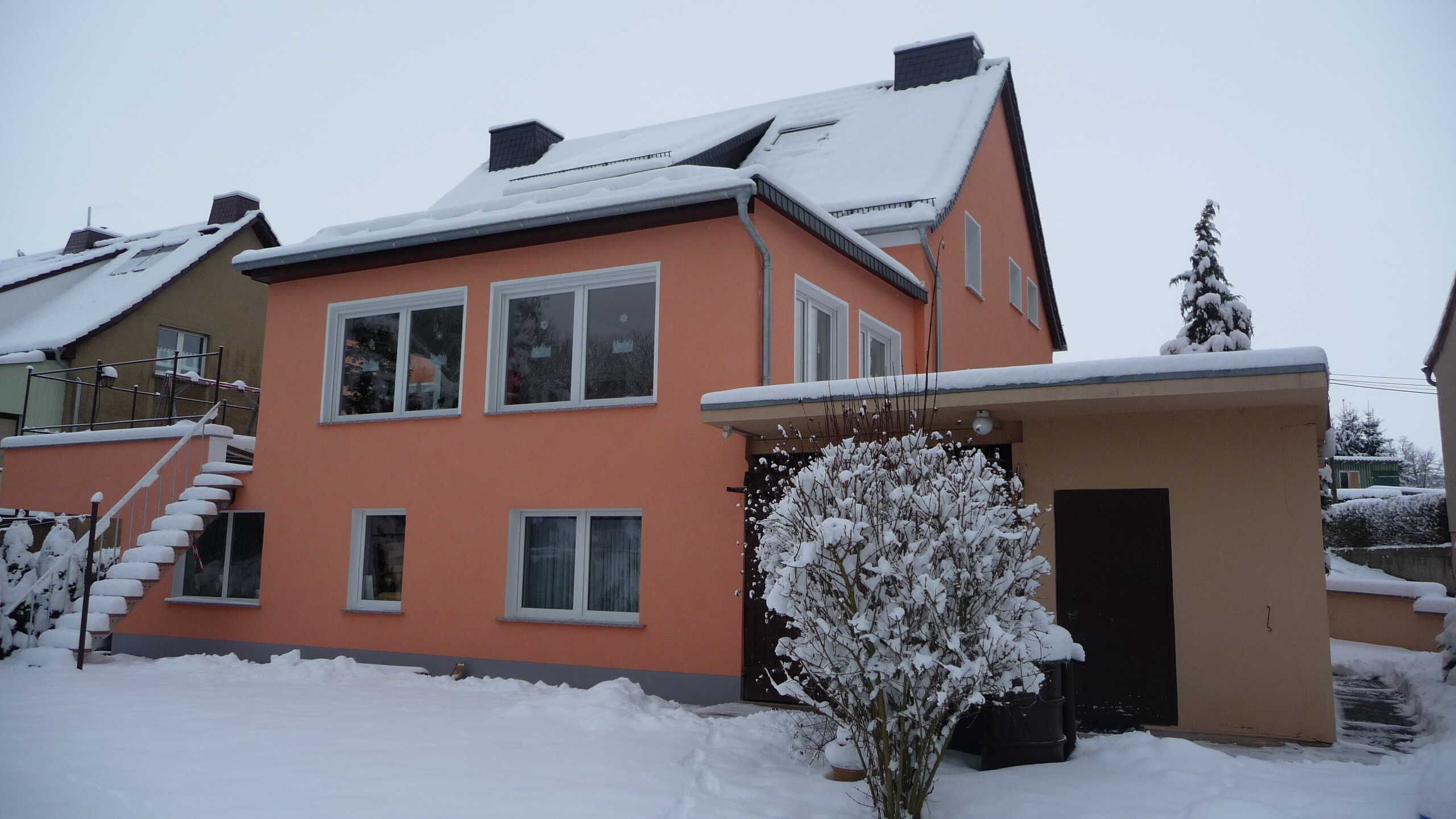 Ein zweistöckiges Haus mit schneebedecktem Dach und einer kleinen angebauten Garage.