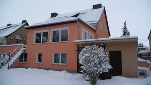 Een huis met twee verdiepingen, een sneeuwbedekte kap en een kleine aangebouwde garage.