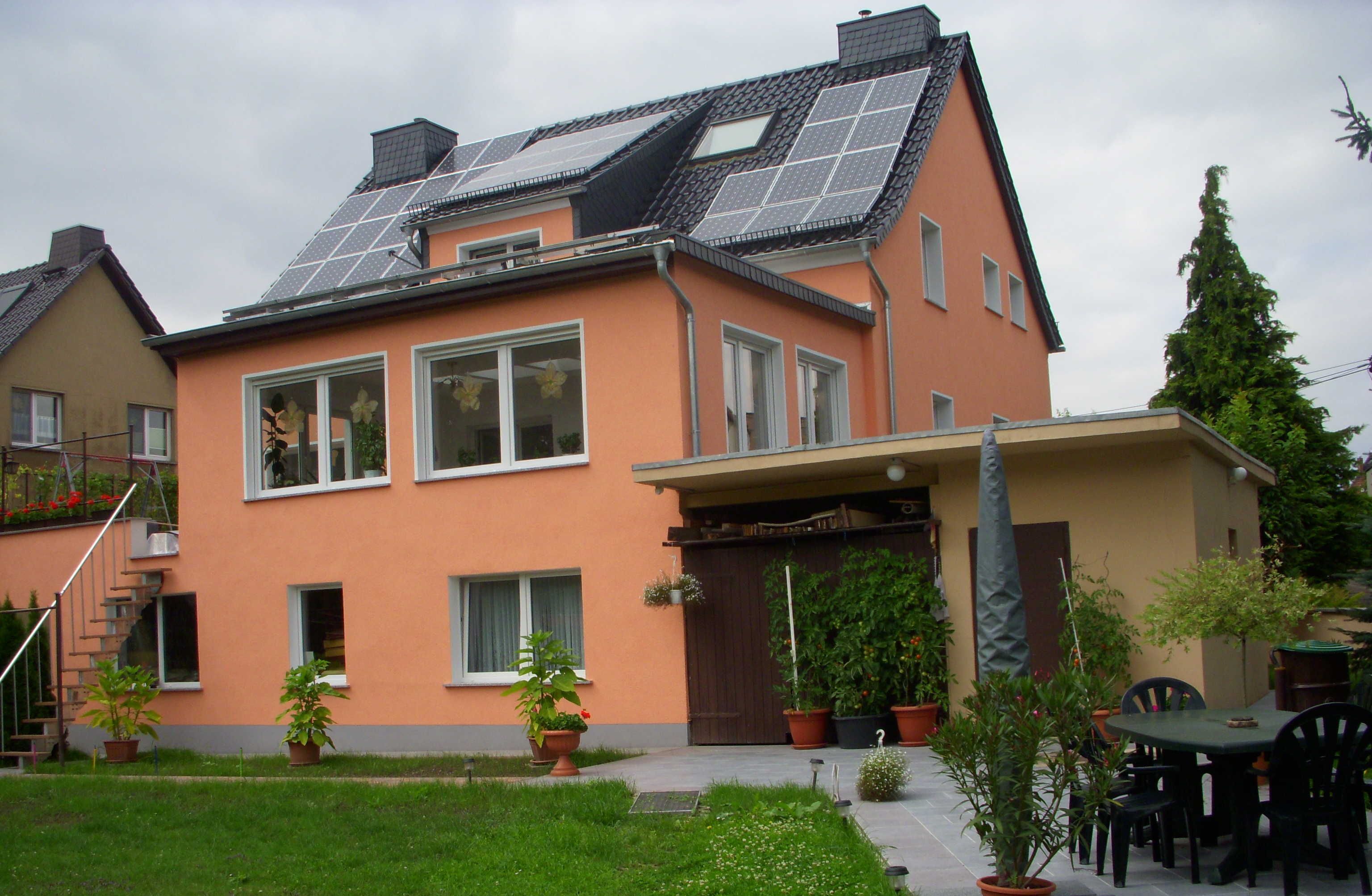 Una casa con paneles solares, un porche cubierto y plantas en macetas.