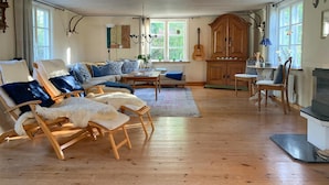 A cozy living room with wooden flooring, a sofa, two armchairs with fur throws, a dining table, and a guitar. - 3 bedroom awesome home in Västervik (Västervik)