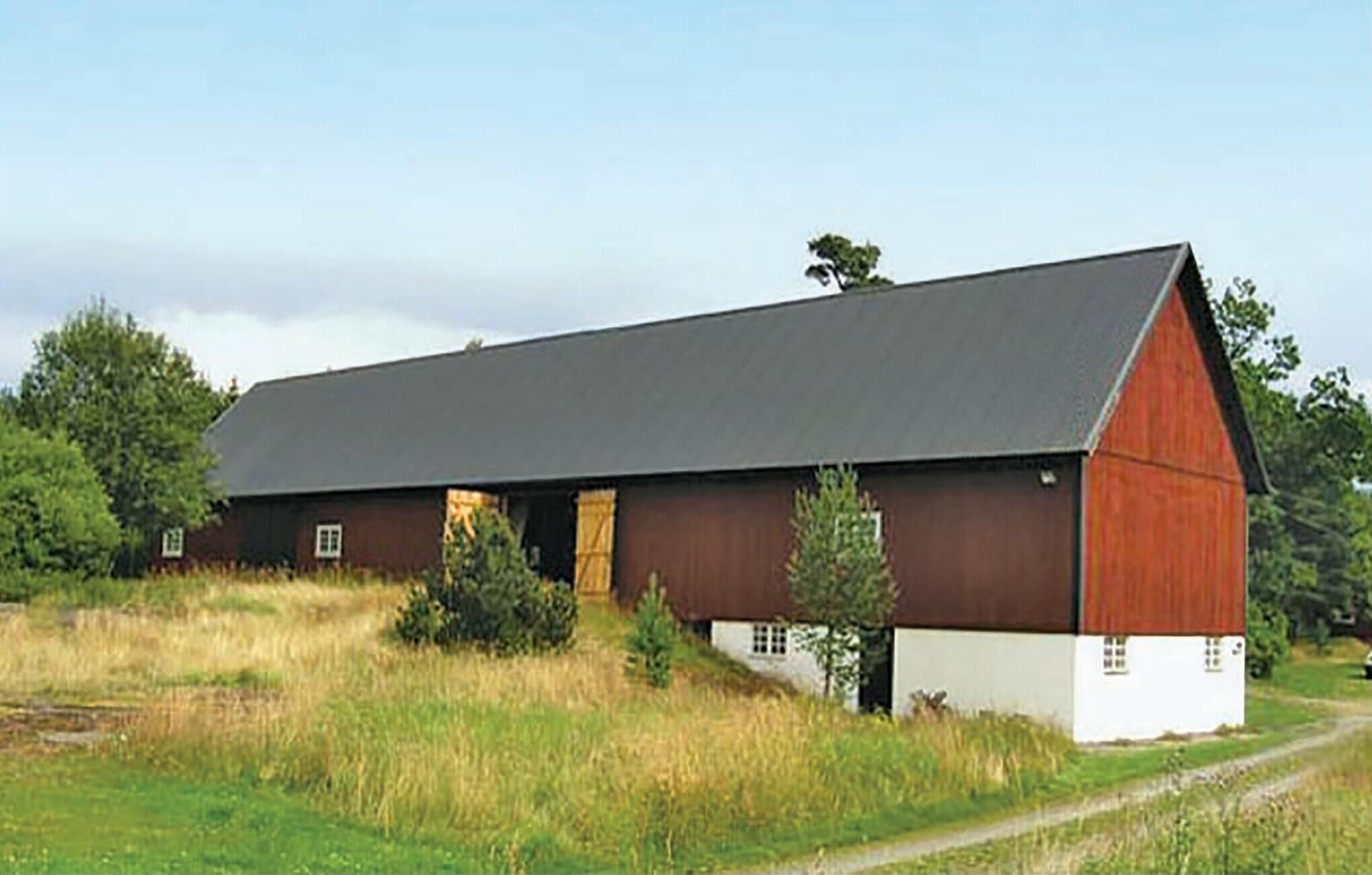 A large, single-story barn with a sloped roof, surrounded by a grassy field and trees.