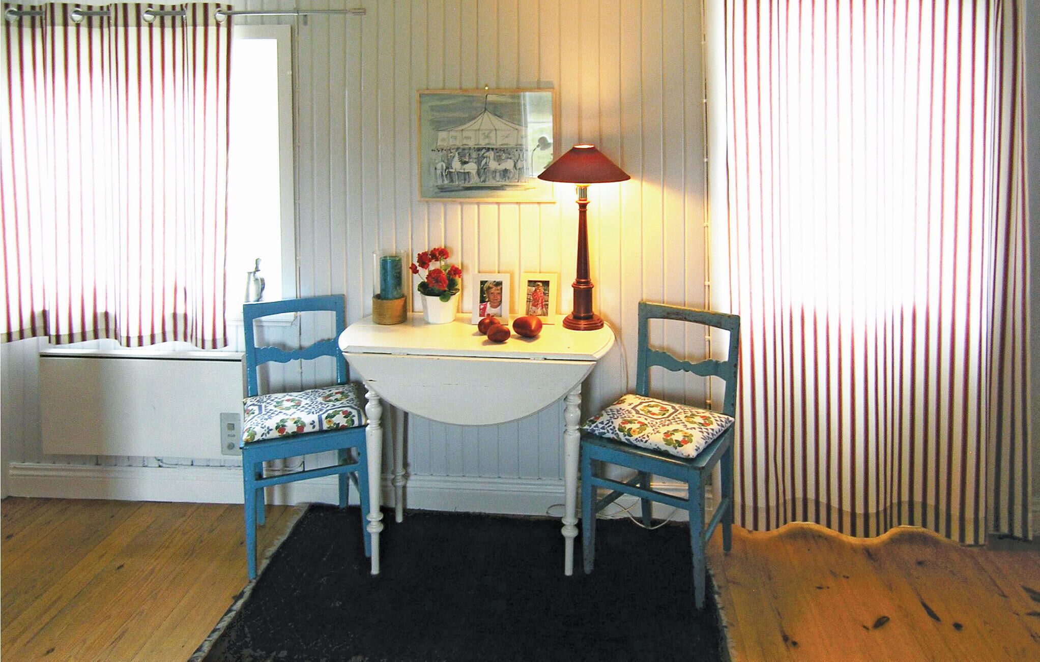A room with two blue chairs, a white table, and a red lamp. There is a framed picture on the wall and a small plant on the table.