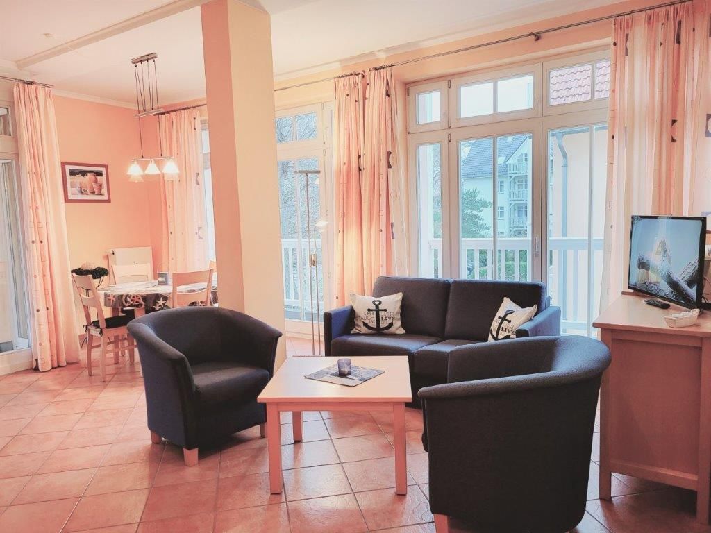 A living room with a sofa, two armchairs, a coffee table, a TV, and a dining area with a table and chairs.