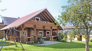 A log cabin with a red-tiled roof, a porch with a railing, and a swing set in the yard. - Cozy home in Harzgerode/Dankerode (Harzgerode/Dankerode)