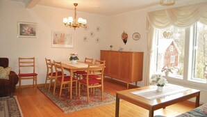 A dining area with a wooden table, red chairs, a chandelier, and a view of a brick building through a window.