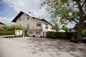 Une maison à deux étages avec un balcon, une allée et un arbre au premier plan.