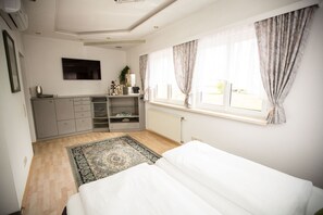 Un dormitorio con cama, cómoda, radiador, ventana con cortinas y televisor en la pared.