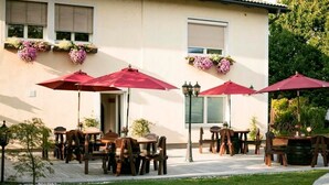 Une terrasse extérieure avec des tables et des chaises en bois, des parasols rouges et des jardinières suspendues.