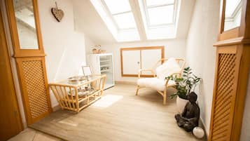 Ein Zimmer mit schrägem Dach, Holzboden, einem weißen Stuhl, einem kleinen Tisch, einer Topfpflanze und einer Statue.