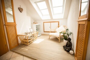 Une pièce avec un plafond en pente, un plancher en bois, une chaise blanche, une petite table, une plante en pot et une statue.