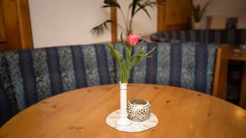 Ein runder Holztisch mit einer weißen Vase, einer rosa Blume, einem gemusterten Kissen und einer dekorativen Schale.