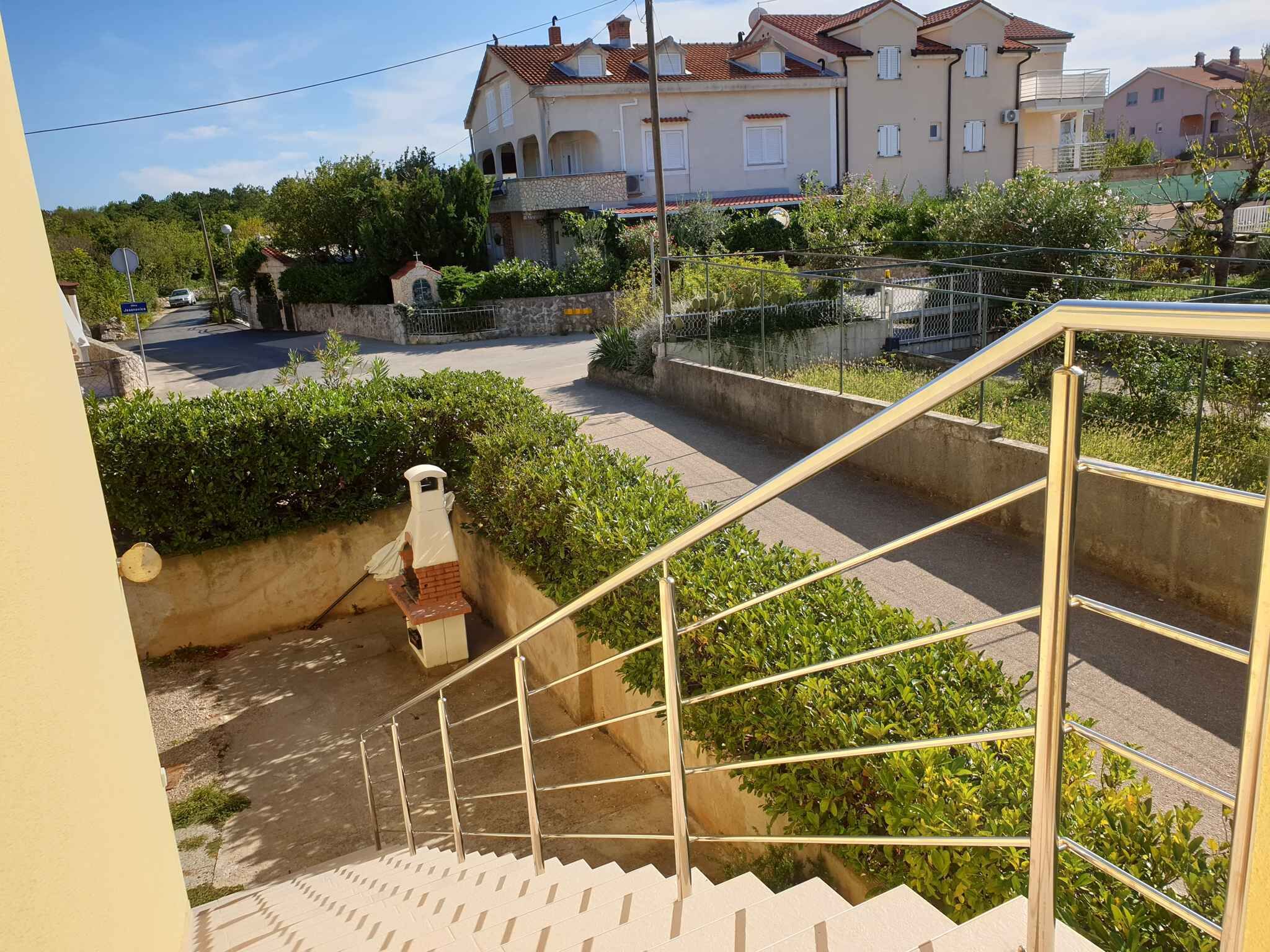 Quartiere residenziale con una scala che conduce a un ingresso chiuso da cancello, circondato da vegetazione e case.