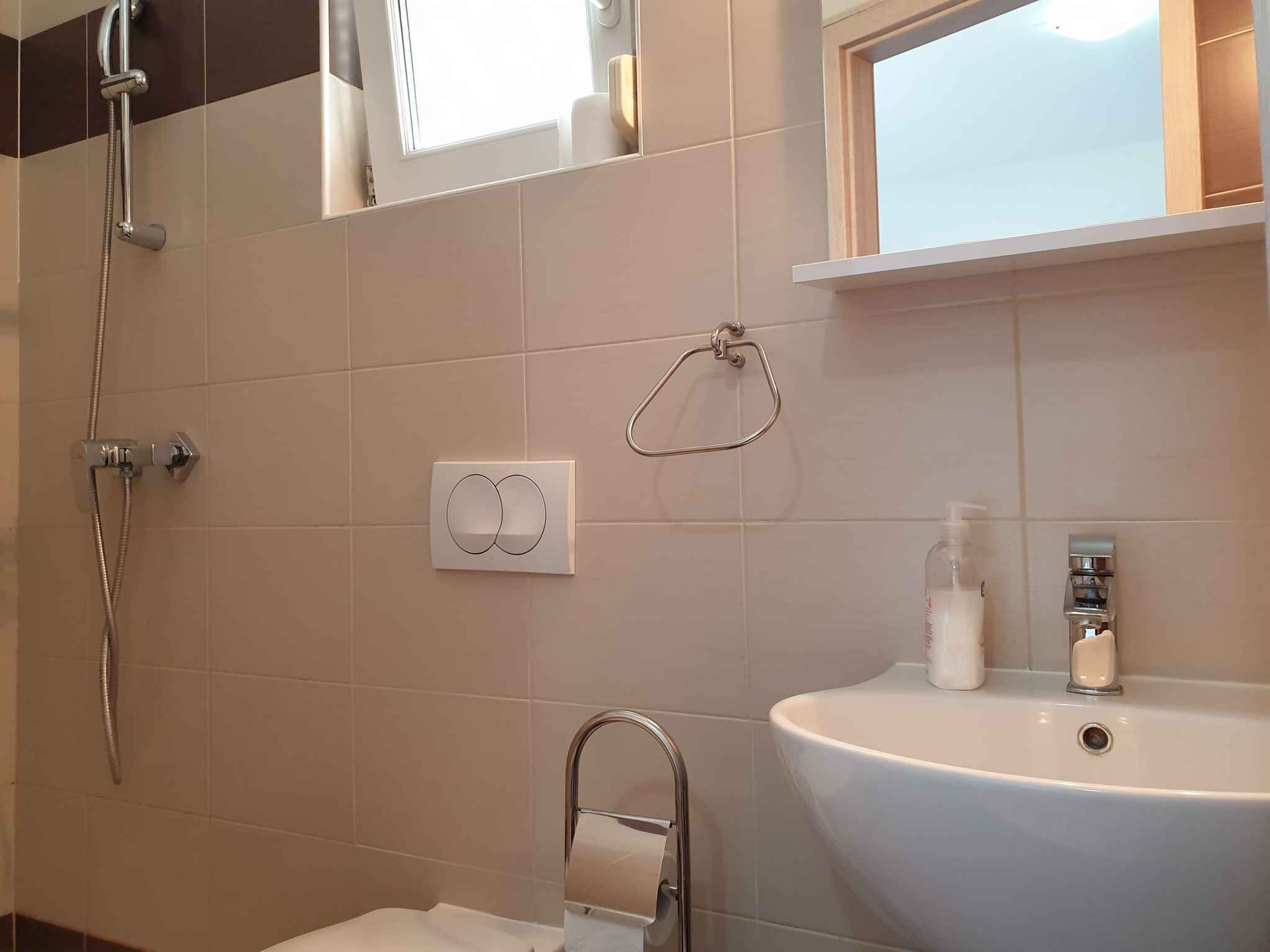 Un baño con ducha, lavamanos, toallero y dispensador de jabón.
