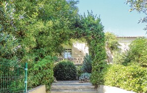 Un chemin de pierres serpente à travers un jardin luxuriant, surmonté d’une arche formée de plantes grimpantes.