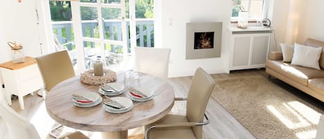 A dining area with a round table set for four, surrounded by chairs. There is a large window with a view of greenery outside.
