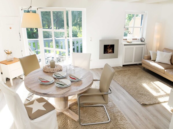 A dining area with a round table set for four, surrounded by chairs. There is a large window with a view of greenery outside.