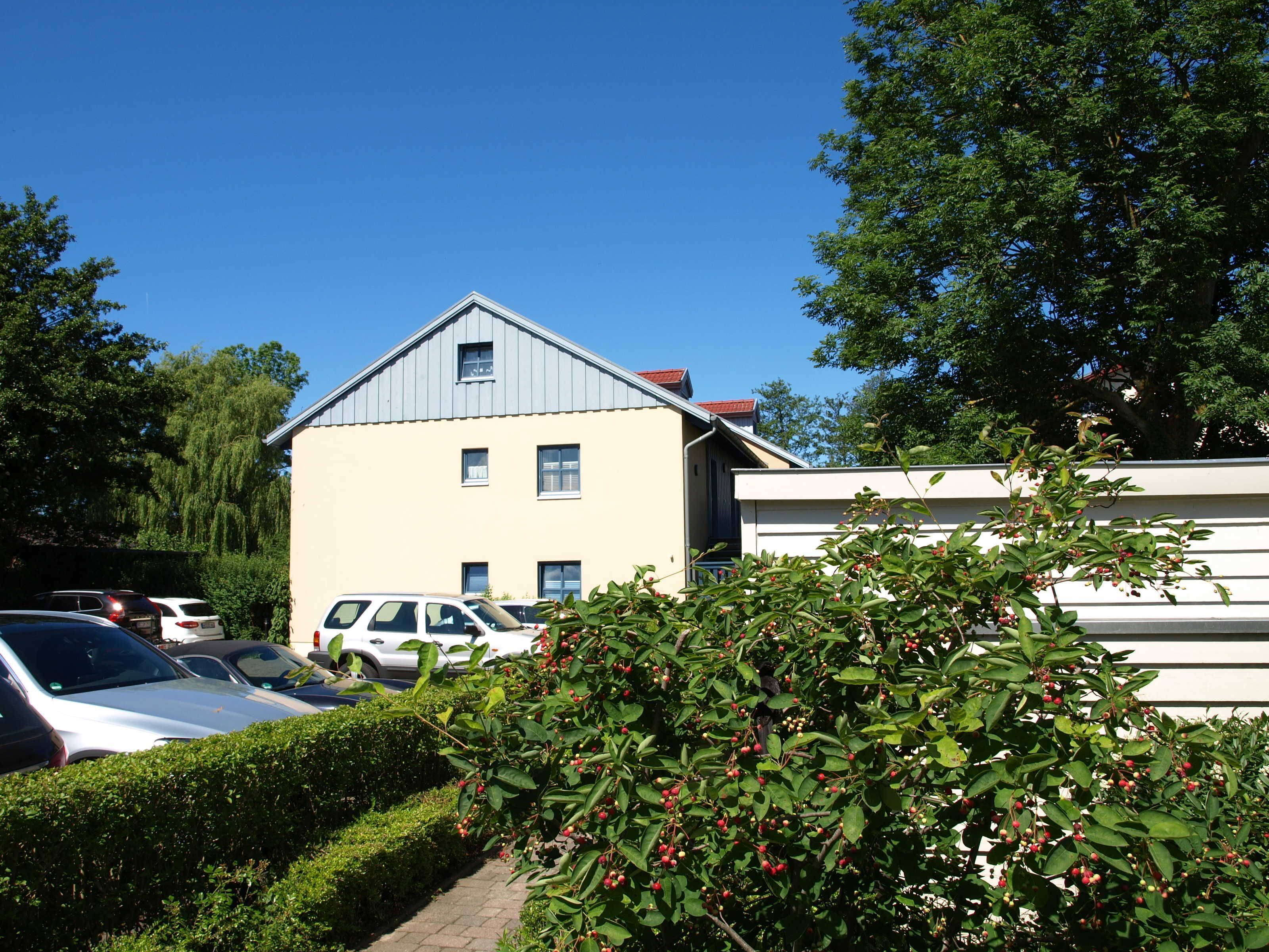 A two-story building with a sloped roof, parked cars, and a bush with red berries in the foreground.
