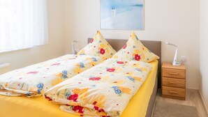 A double bed with floral bedding, a nightstand with a lamp, and a painting on the wall. - FH Herve, Monica GM 69206-FH Cather (Graal-Müritz)