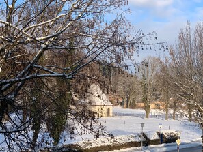 A snow-covered landscape with bare trees and a small building, likely a chapel or historical site, surrounded by a fenced area. - Apartment Ape Maja, Germany (Bad Wiessee)