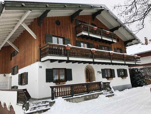 Un chalet en bois à plusieurs étages, doté de balcons, d’une entrée couverte et d’un terrain enneigé.