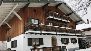 Un chalet en bois à plusieurs étages, doté de balcons, d’une entrée couverte et d’un terrain enneigé.