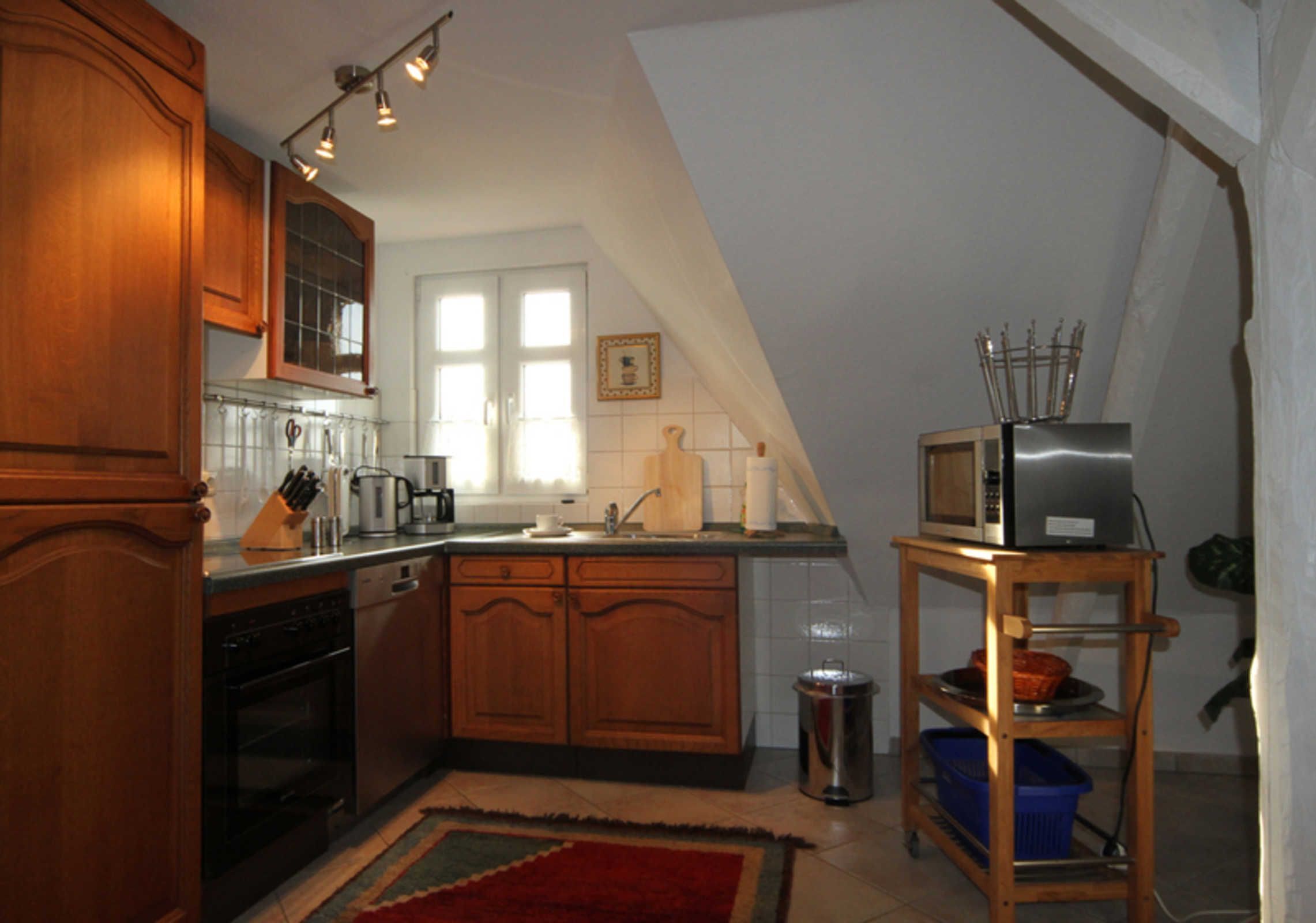 Une cuisine avec des meubles de rangement en bois, une cuisinière, un évier et un four à micro-ondes posé sur une étagère en bois.