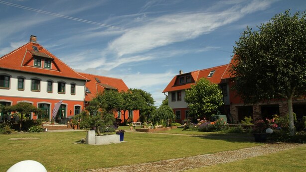 Ein Innenhof mit zwei Gebäuden mit roten Dächern, einem gepflegten Rasen und blauem Himmel.