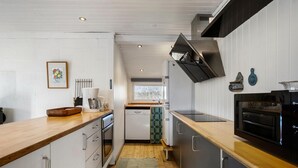 Une cuisine moderne avec des meubles blancs, un plan de travail en bois, un lave-vaisselle, une cuisinière et une fenêtre qui laisse entrer la lumière naturelle.