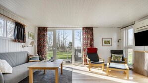 Un salon spacieux avec un canapé gris, deux fauteuils, une table basse en bois et un téléviseur.