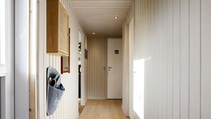 Un couloir étroit, doté d’un plancher en bois et de murs blancs, qui mène à une porte sur laquelle est apposé un panneau indiquant les toilettes.