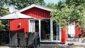 Un bâtiment rouge avec une entrée dotée d’une porte en verre, des meubles en osier et un foyer extérieur.