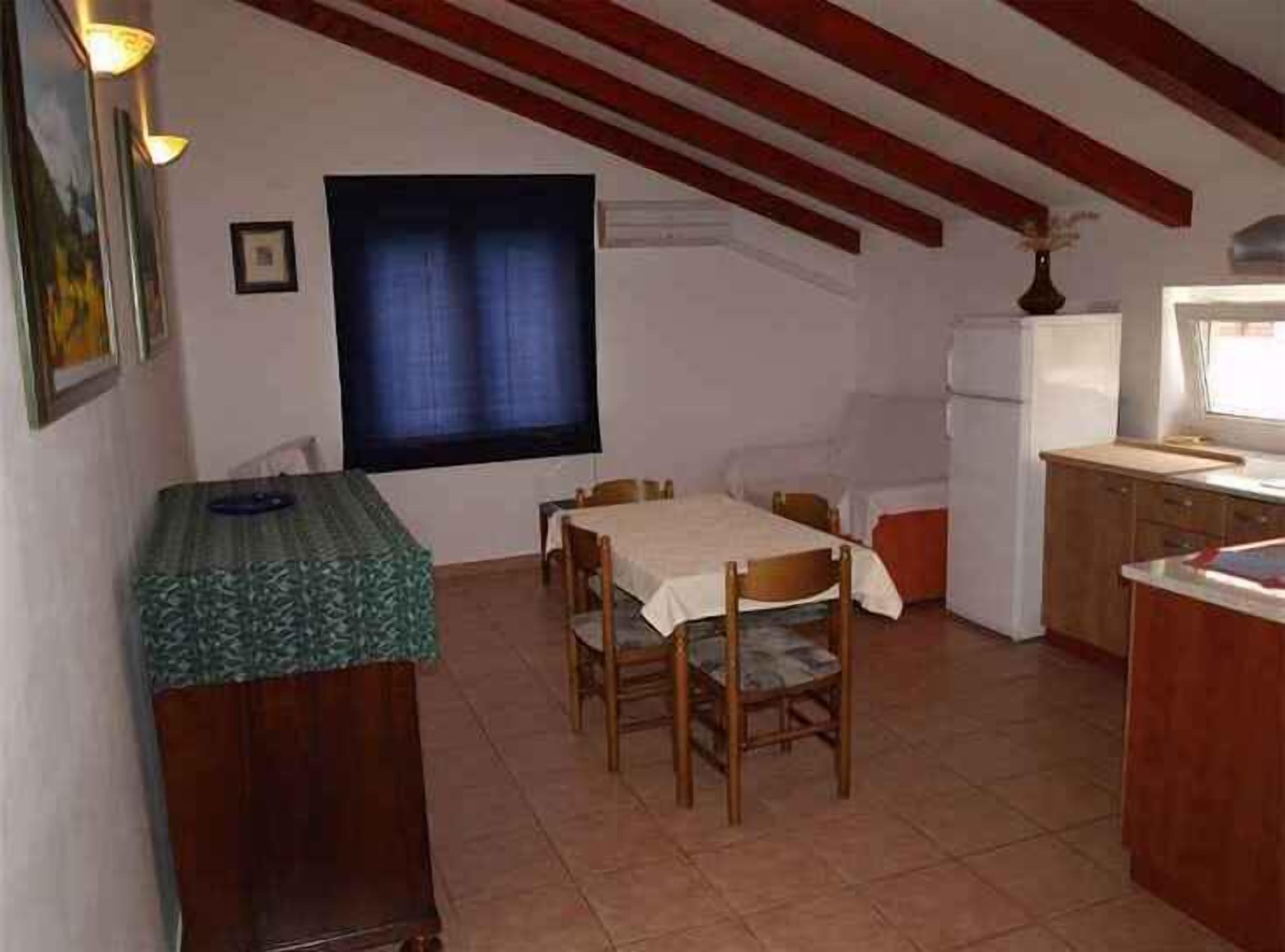 Une petite cuisine équipée d’une table et de chaises, d’un réfrigérateur et d’une fenêtre avec des rideaux.