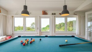 A pool table with balls, two pendant lights, and windows with a view of greenery. - 4 bedroom amazing home in Ebeltoft (Ebeltoft)