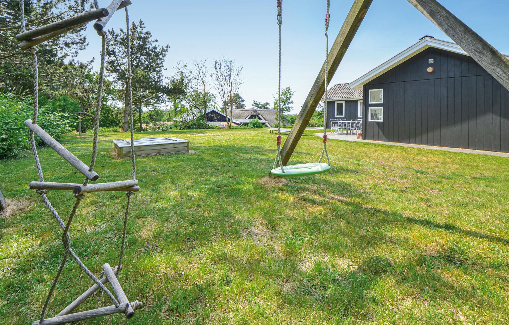 A grassy outdoor area with a swing set, a wooden bench, and a building with a dark exterior.