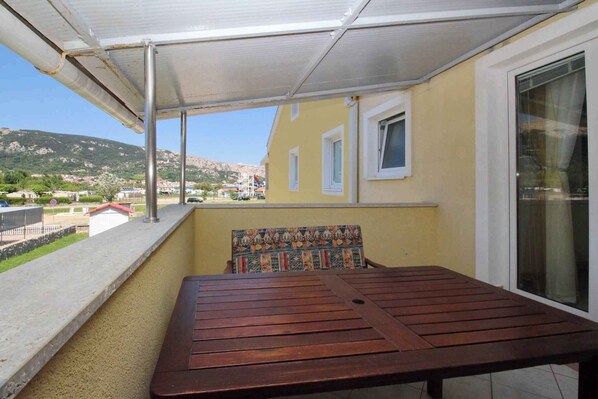 Un balcón con una mesa de madera y un banco estampado, con vistas a una zona residencial con casas y colinas.