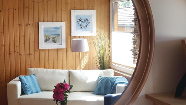 A room with a wooden paneled wall, a white sofa with blue cushions, a lamp, and two framed pictures. - 2 bedroom amazing home in Thale/Friedrichsbrunn (Thale/Friedrichsbrunn)