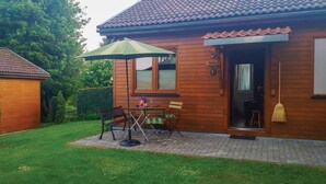 A wooden house with a tiled roof, a patio with a table and chairs, and a green umbrella. - 2 bedroom amazing home in Thale/Friedrichsbrunn (Thale/Friedrichsbrunn)