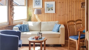 A cozy room with a wooden paneled wall, a beige sofa with blue cushions, a wooden chair with a blue cushion, and a small wooden table with a bowl of fruit. - 2 bedroom amazing home in Thale/Friedrichsbrunn (Thale/Friedrichsbrunn)