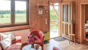 A wooden interior with a sofa, a red chair, a small table with flowers, and a view of a green landscape through large windows. - 2 bedroom amazing home in Thale/Friedrichsbrunn (Thale/Friedrichsbrunn)