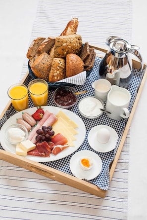 Un plateau de petit-déjeuner contenant divers aliments et boissons, notamment du pain, du fromage, de la charcuterie et des fruits.