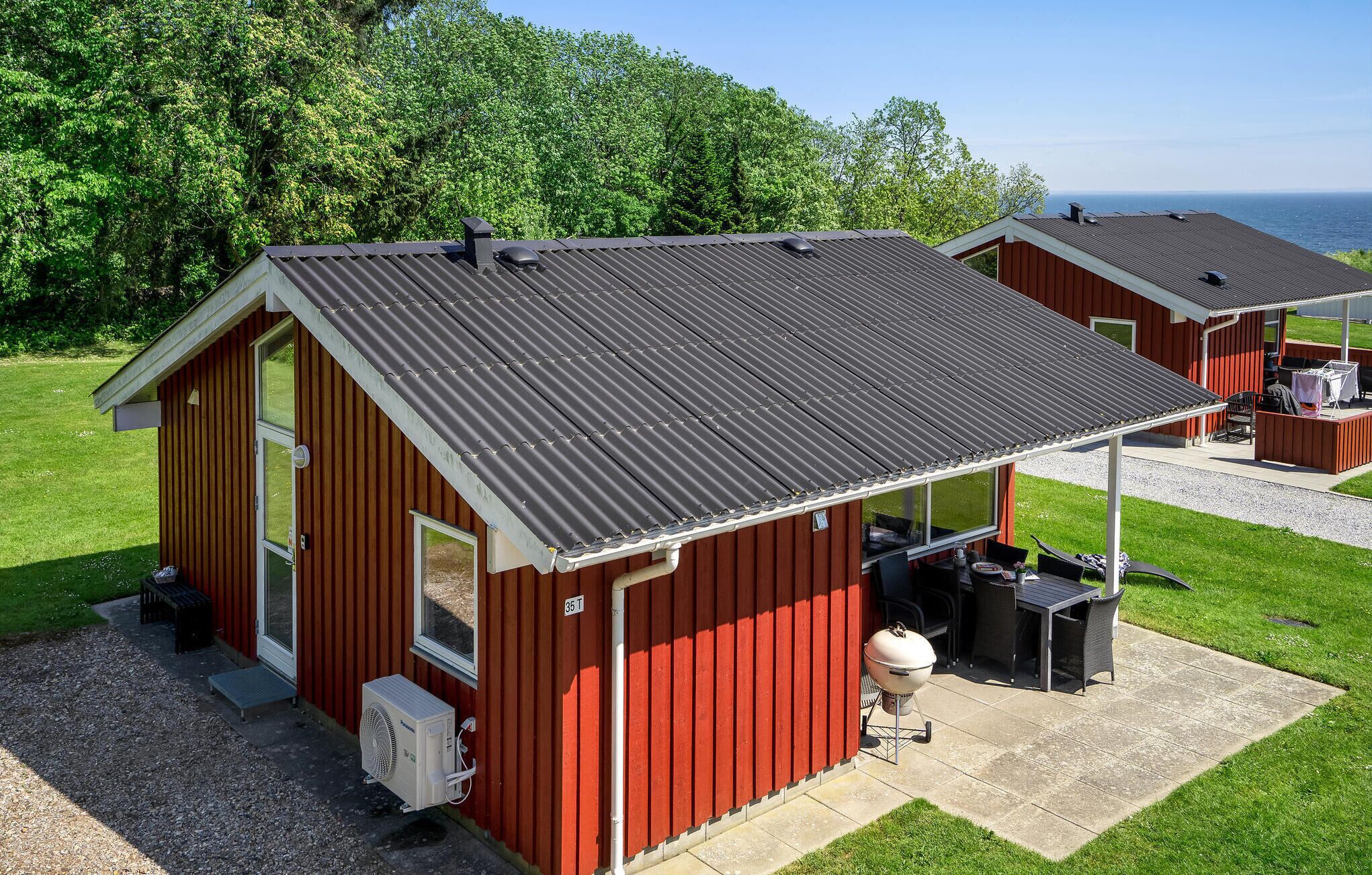 Un bâtiment en métal rouge doté d’un patio couvert, d’un barbecue et offrant une vue sur l’océan.